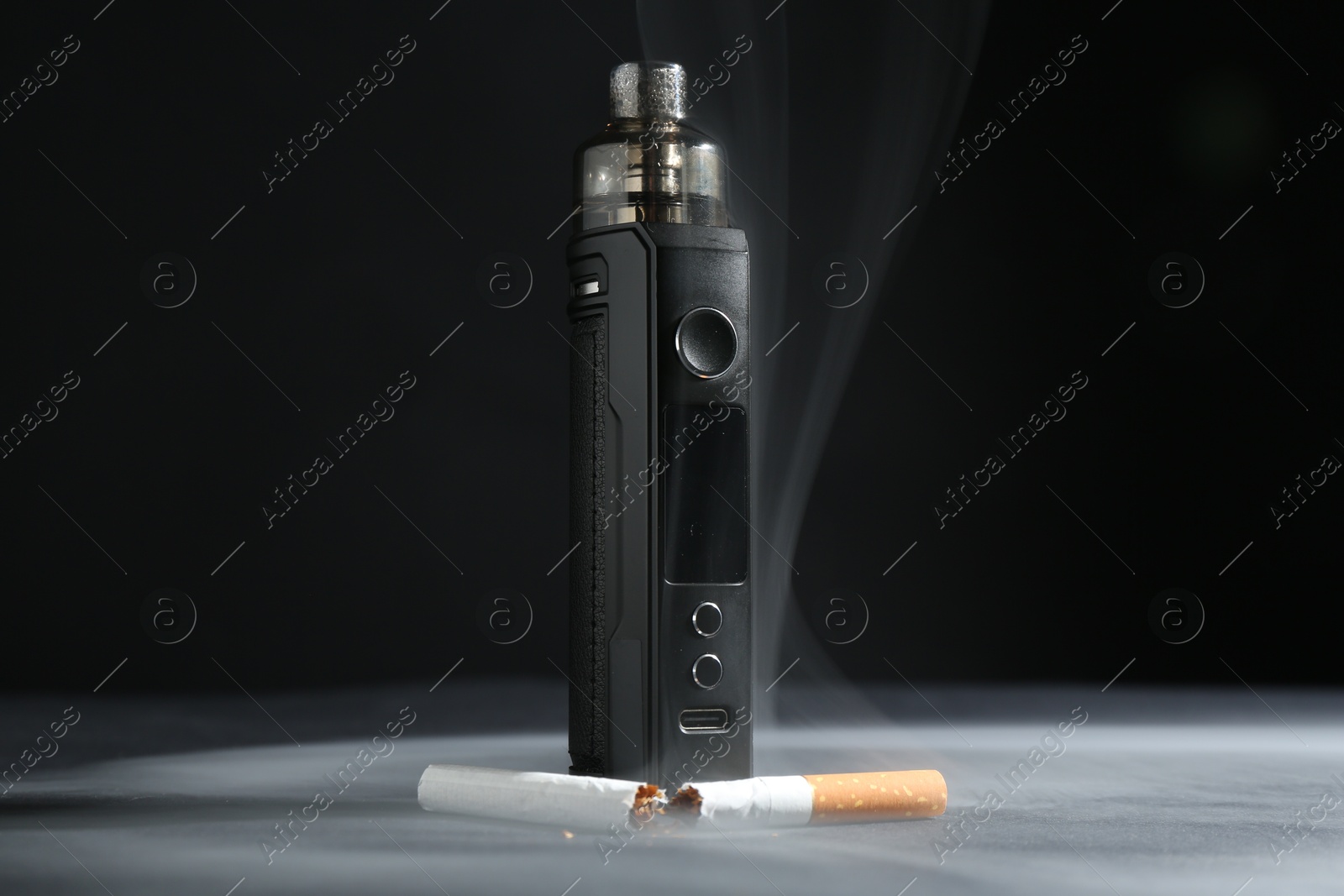 Electronic smoking device and broken cigarette in smoke on dark table against black background, closeup Photo of Electronic smoking device and broken cigarette in smoke on dark table against black background, closeup