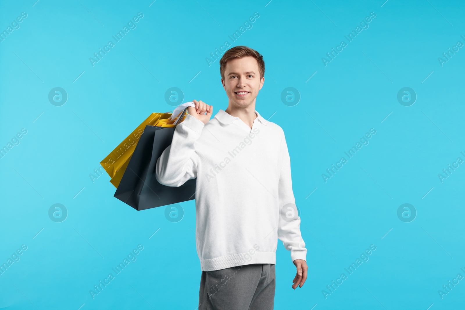 Cheerful man with shopping bags on light blue background Photo of Cheerful man with shopping bags on light blue background