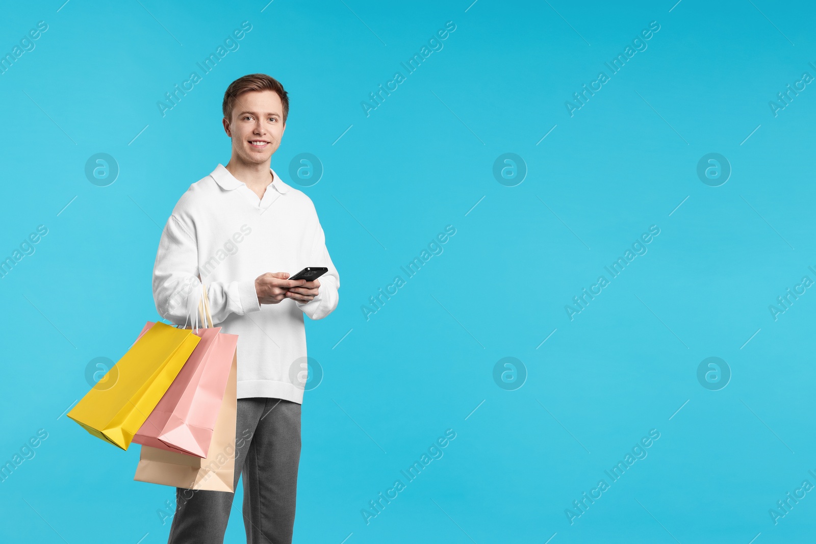 Cheerful man with smartphone and shopping bags on light blue background. Space for text Photo of Cheerful man with smartphone and shopping bags on light blue background. Space for text