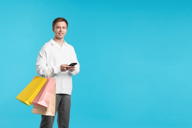 Photo of Cheerful man with smartphone and shopping bags on light blue background. Space for text
