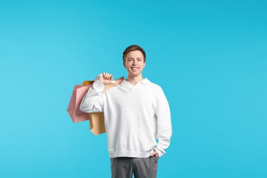 Photo of Cheerful man with shopping bags on light blue background