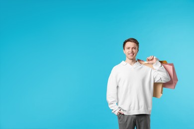 Photo of Cheerful man with shopping bags on light blue background. Space for text