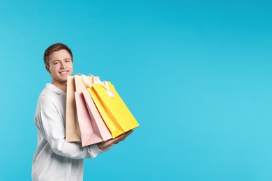 Photo of Cheerful man with shopping bags on light blue background. Space for text