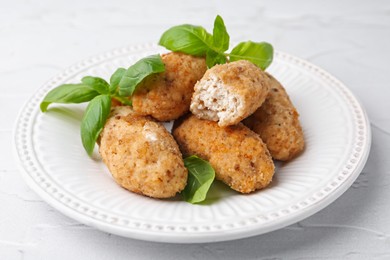 Photo of Tasty fried croquettes and basil on white textured table, closeup