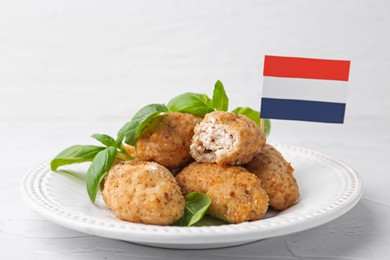 Photo of Tasty fried croquettes, basil and flag of Netherlands on white textured table, closeup