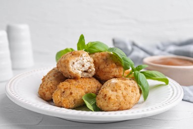 Photo of Tasty fried croquettes, basil and sauce on white textured table, closeup