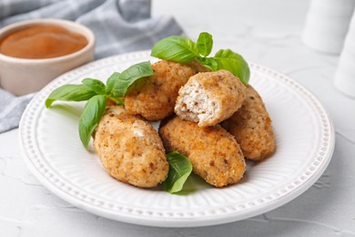 Photo of Tasty fried croquettes, basil and sauce on white textured table, closeup