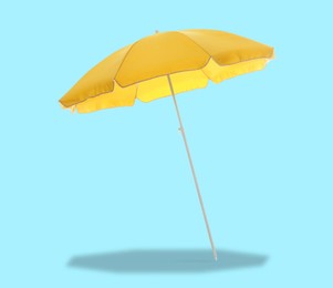 Image of Yellow beach umbrella casting shadow on light blue background