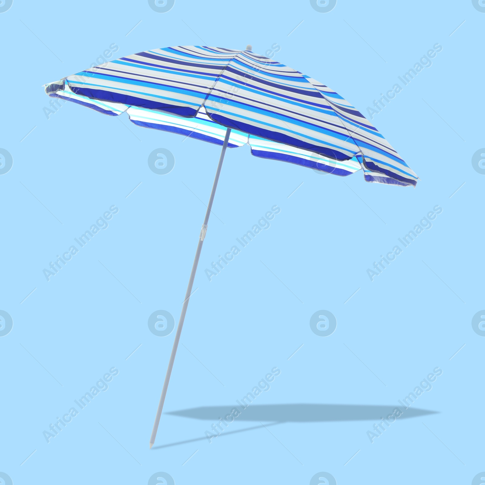 Image of Blue striped beach umbrella casting shadow on light blue background