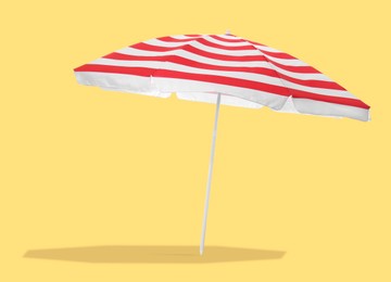 Image of Red striped beach umbrella casting shadow on yellow background