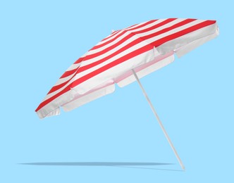 Image of Red striped beach umbrella casting shadow on light blue background