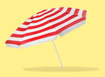 Image of Red striped beach umbrella casting shadow on yellow background