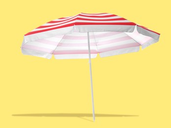 Image of Red striped beach umbrella casting shadow on yellow background