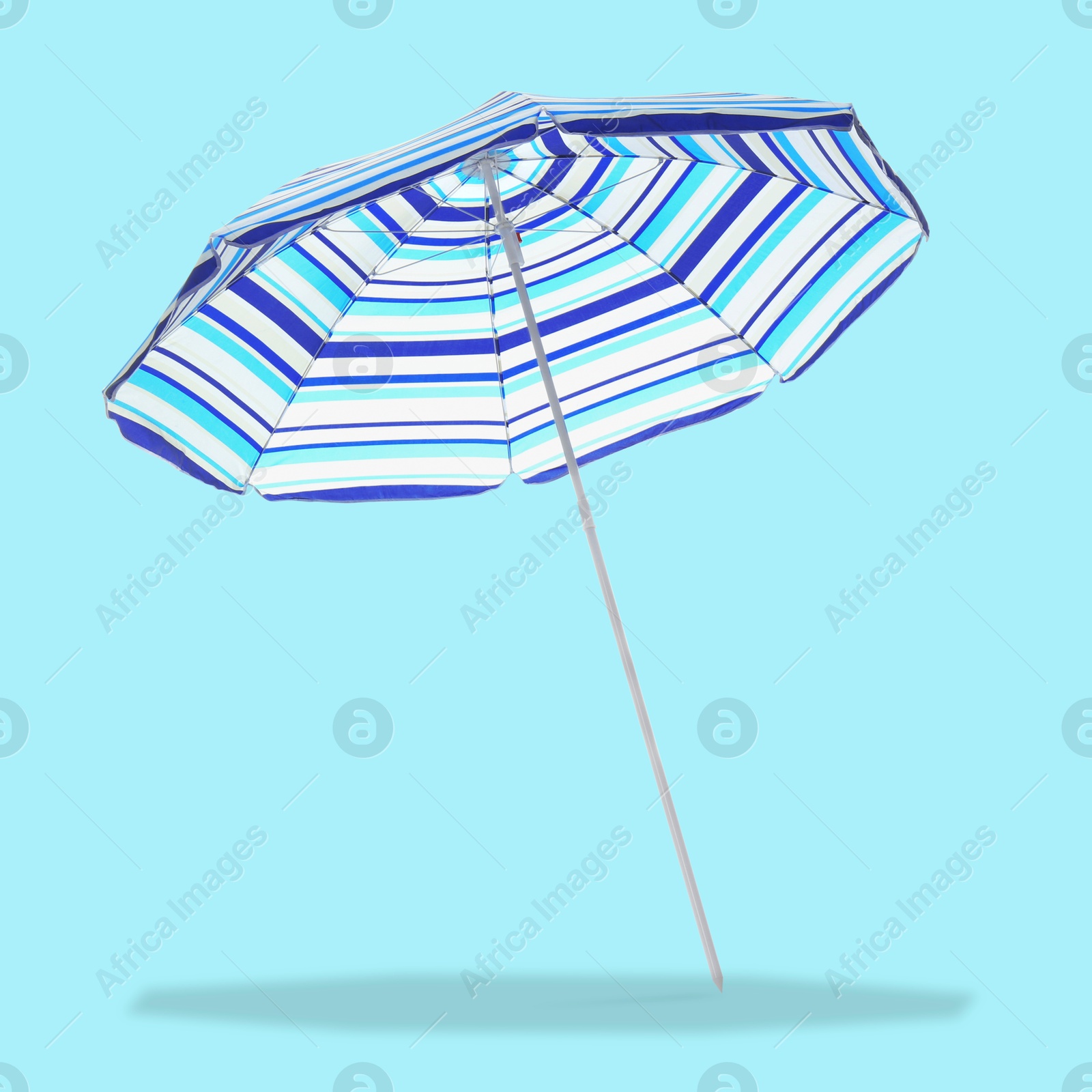 Image of Blue striped beach umbrella casting shadow on light blue background