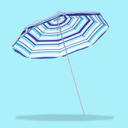 Image of Blue striped beach umbrella casting shadow on light blue background