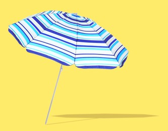 Image of Blue striped beach umbrella casting shadow on yellow background