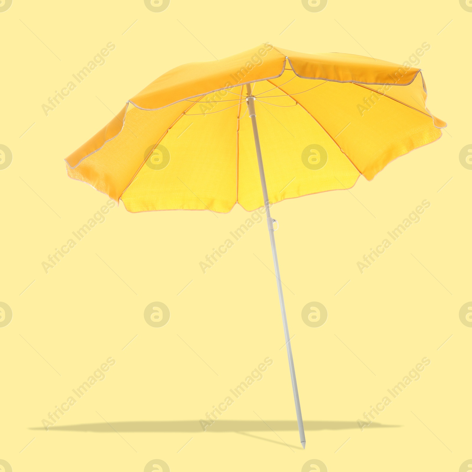 Image of Bright beach umbrella casting shadow on pale yellow background