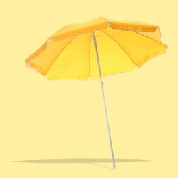 Image of Bright beach umbrella casting shadow on pale yellow background