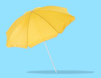 Image of Yellow beach umbrella casting shadow on light blue background