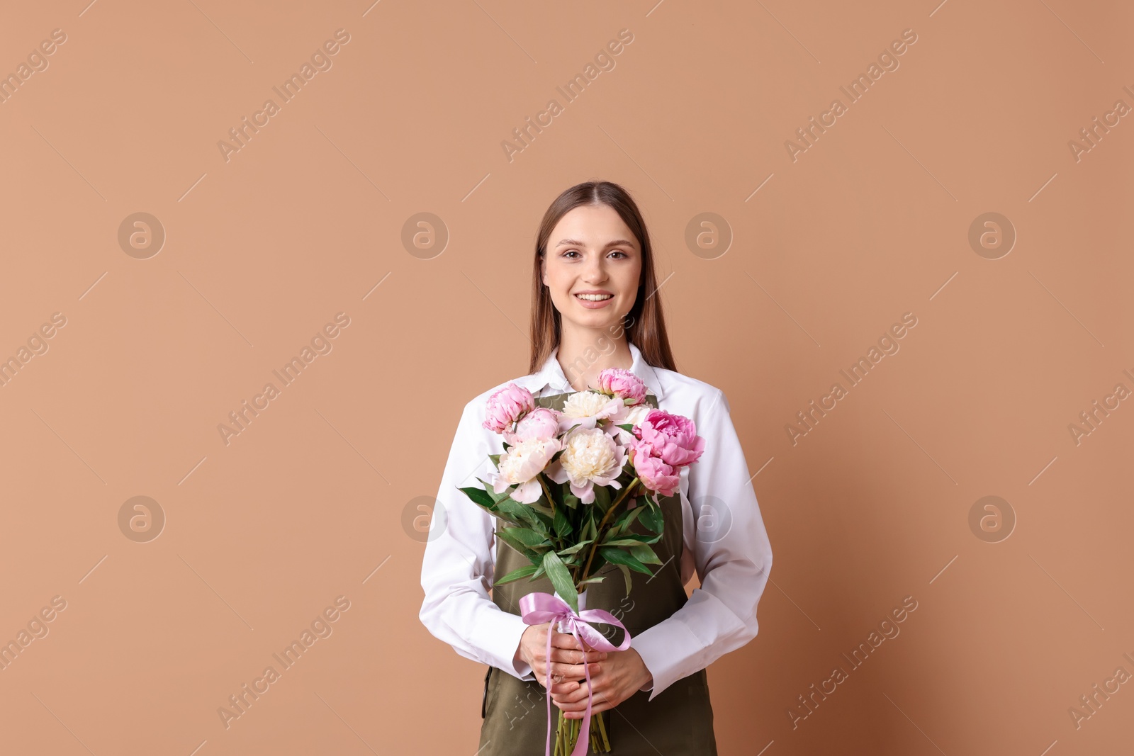 Florist with beautiful bouquet of peonies on dark beige background Photo of Florist with beautiful bouquet of peonies on dark beige background