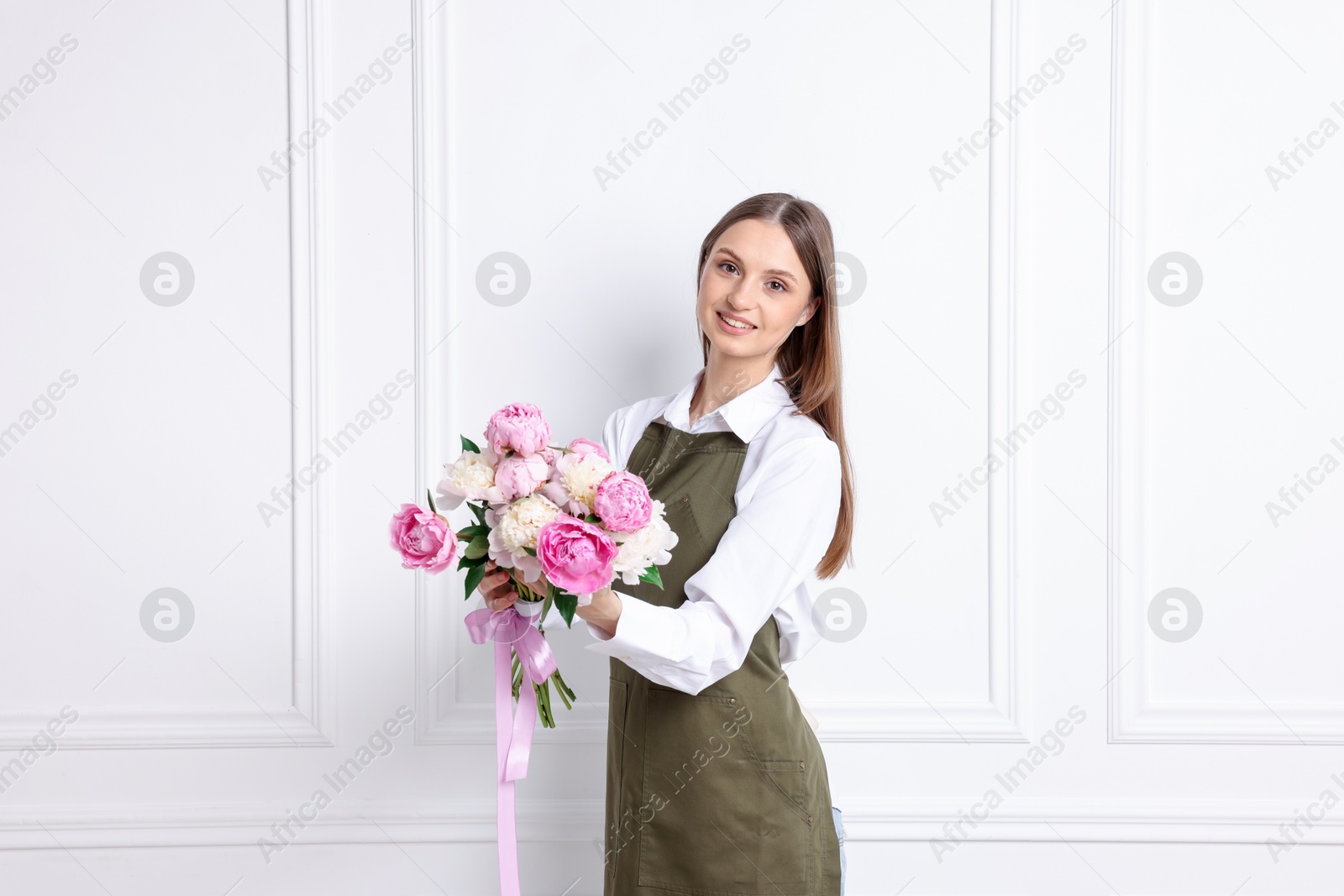 Florist with beautiful bouquet of peonies near white wall indoors Photo of Florist with beautiful bouquet of peonies near white wall indoors
