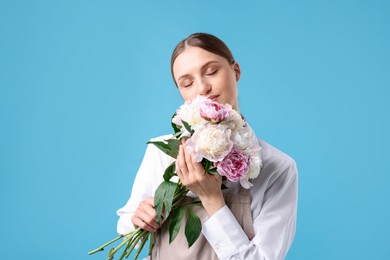 Photo of Florist with beautiful bouquet of peonies on light blue background