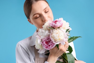 Photo of Florist with beautiful bouquet of peonies on light blue background