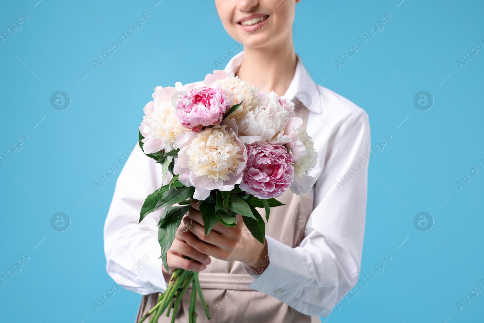 Florist with beautiful bouquet of peonies on light blue background, closeup Photo of Florist with beautiful bouquet of peonies on light blue background, closeup