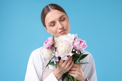 Photo of Florist with beautiful bouquet of peonies on light blue background