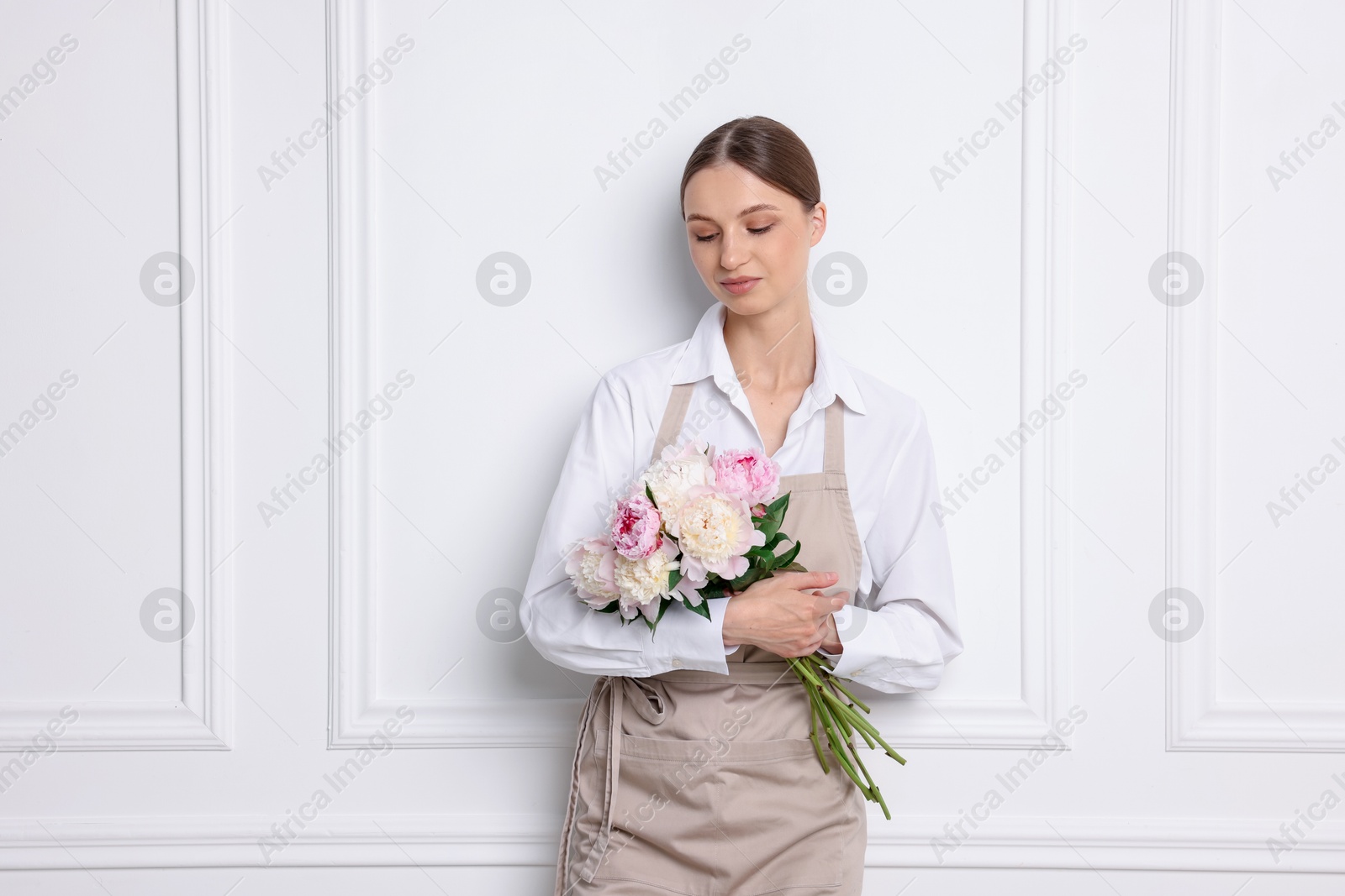 Florist with beautiful bouquet of peonies near white wall indoors Photo of Florist with beautiful bouquet of peonies near white wall indoors