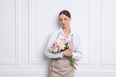 Photo of Florist with beautiful bouquet of peonies near white wall indoors