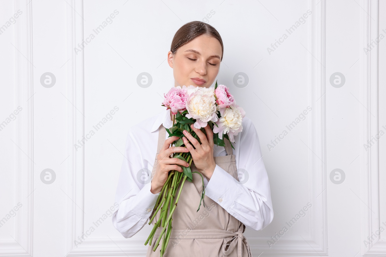 Florist with beautiful bouquet of peonies near white wall indoors Photo of Florist with beautiful bouquet of peonies near white wall indoors
