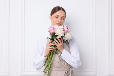 Photo of Florist with beautiful bouquet of peonies near white wall indoors