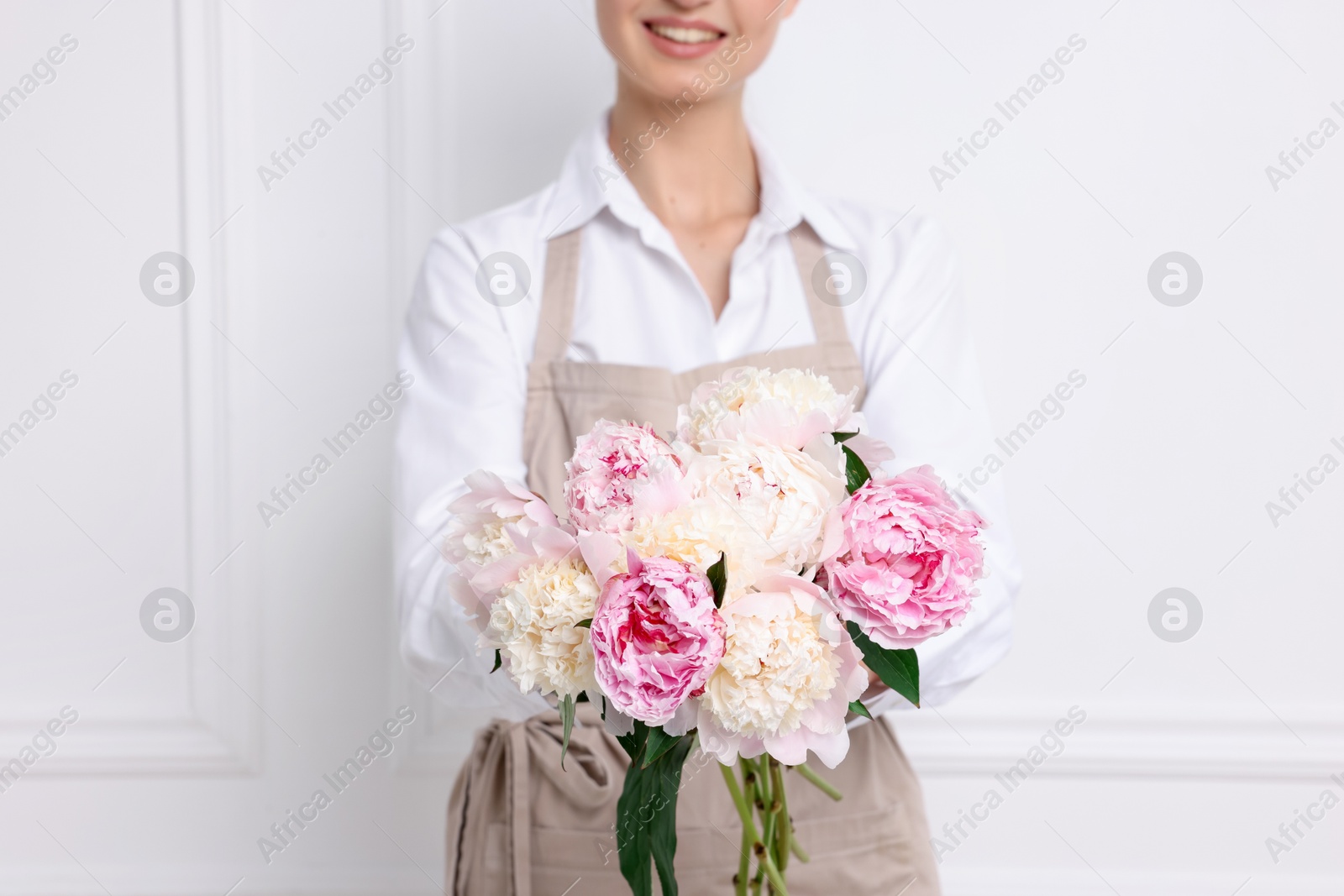 Florist with beautiful bouquet of peonies near white wall indoors, closeup Photo of Florist with beautiful bouquet of peonies near white wall indoors, closeup