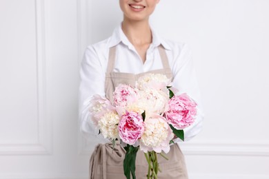 Photo of Florist with beautiful bouquet of peonies near white wall indoors, closeup