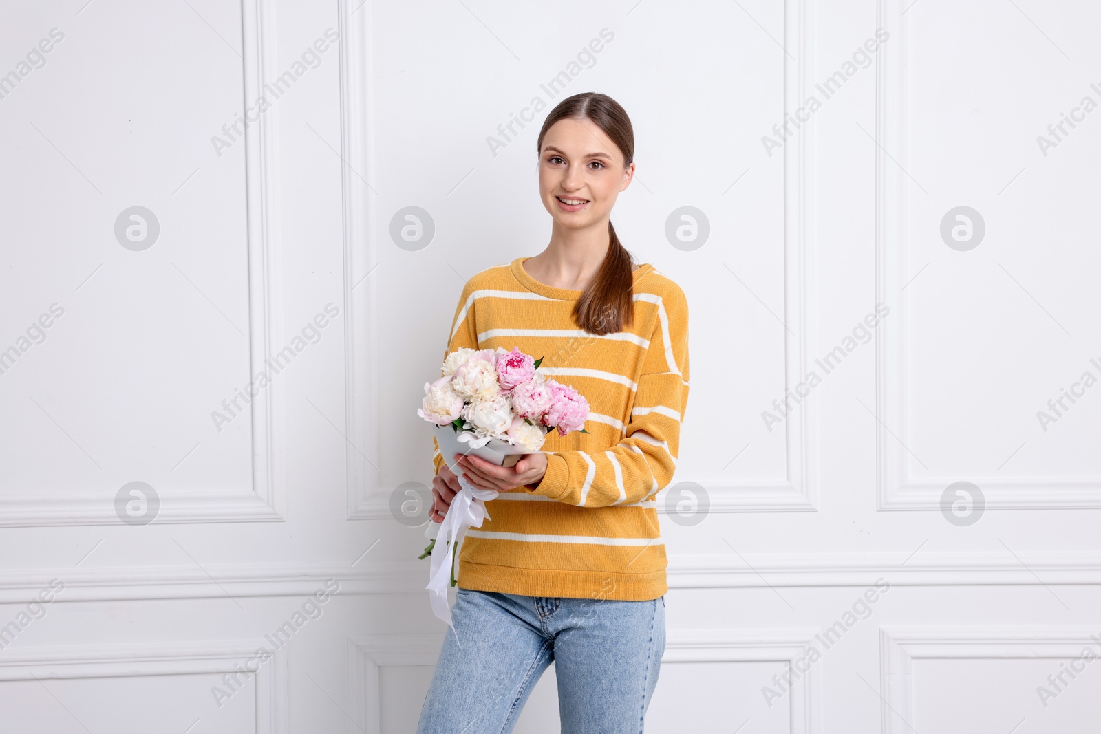 Woman with beautiful bouquet of peonies near white wall indoors Photo of Woman with beautiful bouquet of peonies near white wall indoors
