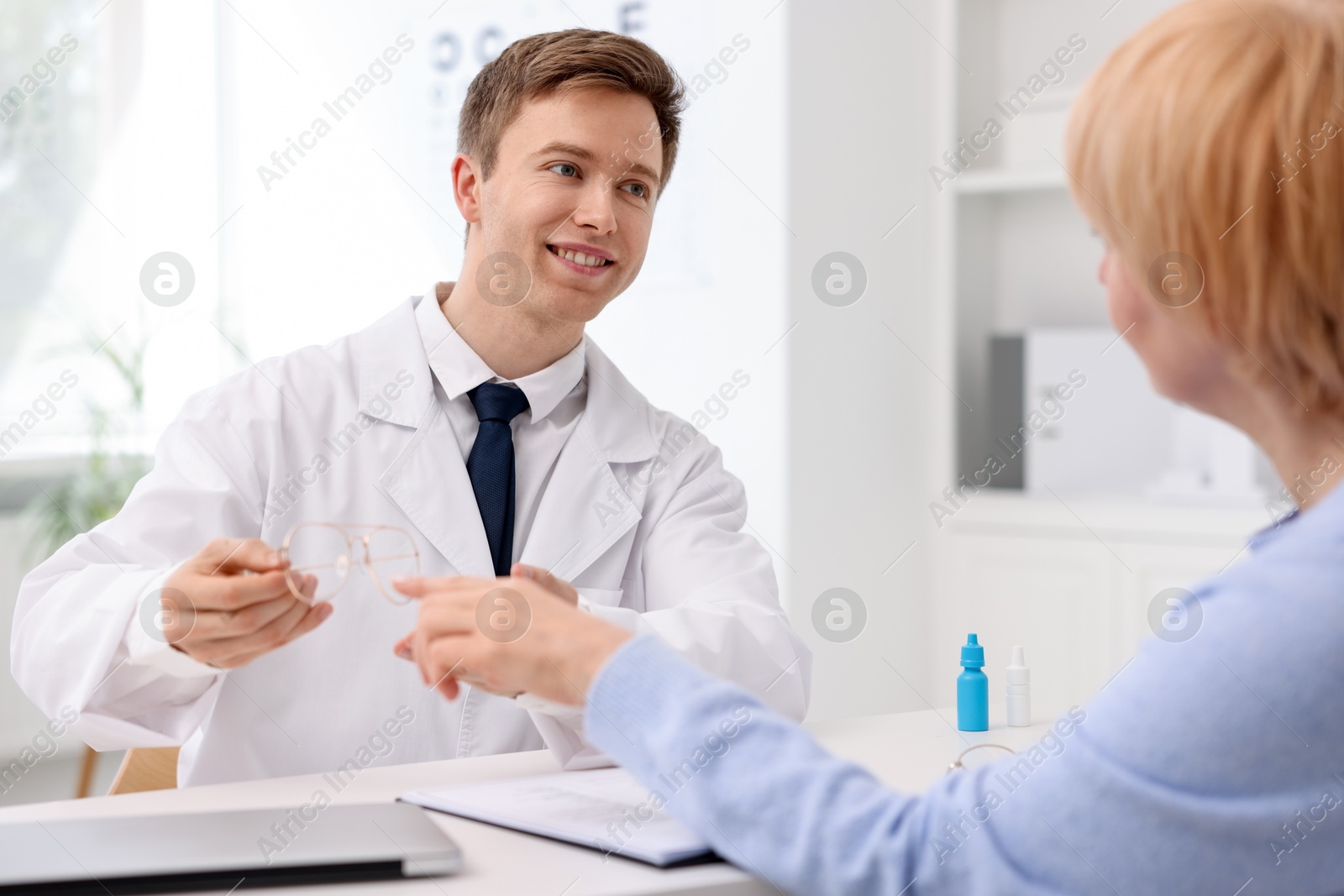 Ophthalmologist consulting senior woman at white table in clinic Photo of Ophthalmologist consulting senior woman at white table in clinic