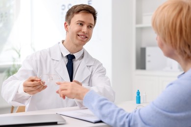 Photo of Ophthalmologist consulting senior woman at white table in clinic