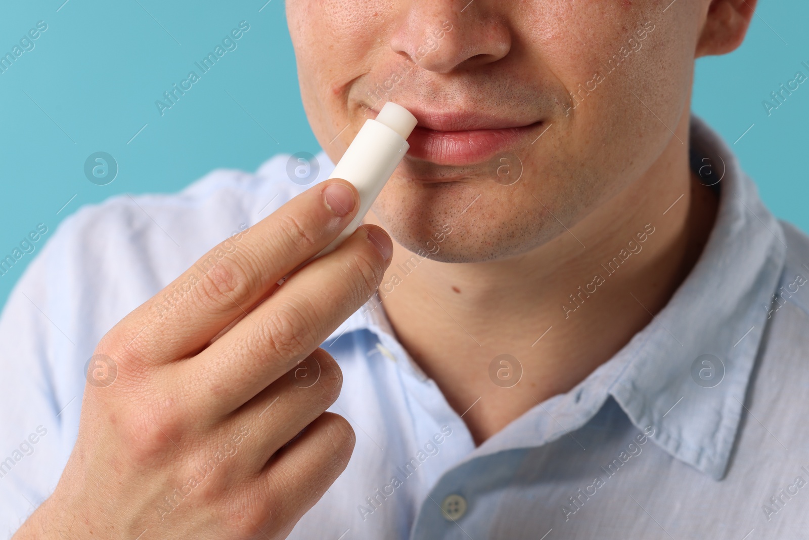 Young man applying lip balm onto his lips on light blue background, closeup Photo of Young man applying lip balm onto his lips on light blue background, closeup