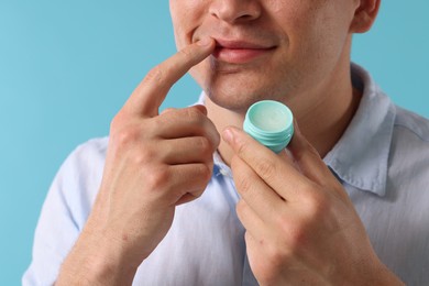 Photo of Young man applying lip balm onto his lips on light blue background, closeup