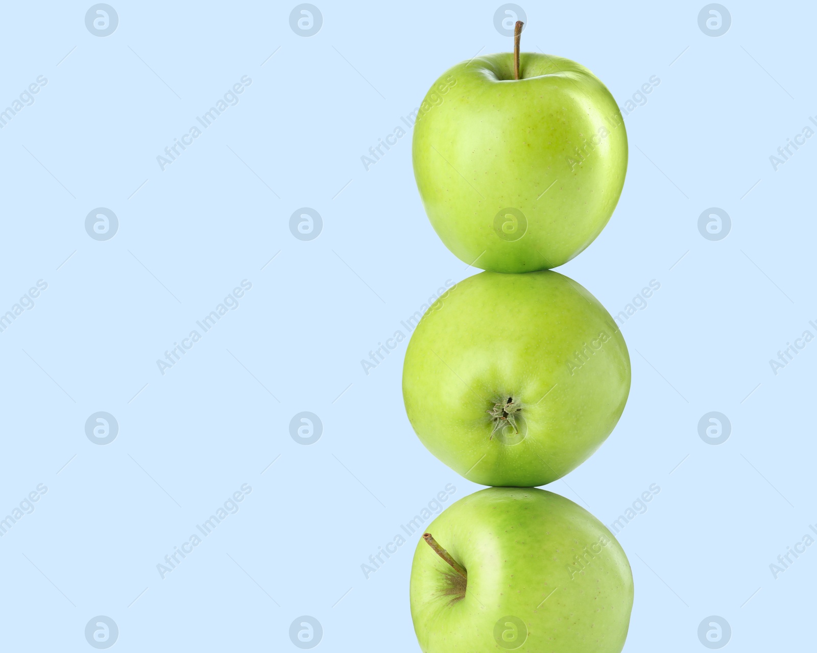Image of Green apples stacked on top of each other against light blue background. Balance
