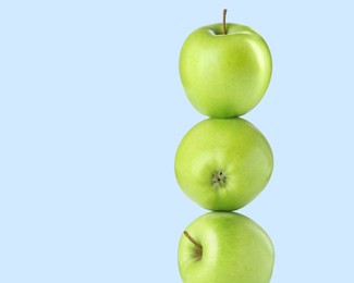 Image of Green apples stacked on top of each other against light blue background. Balance