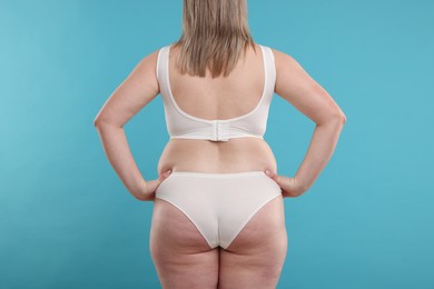 Photo of Weight loss. Plus size woman in underwear on light blue background, back view