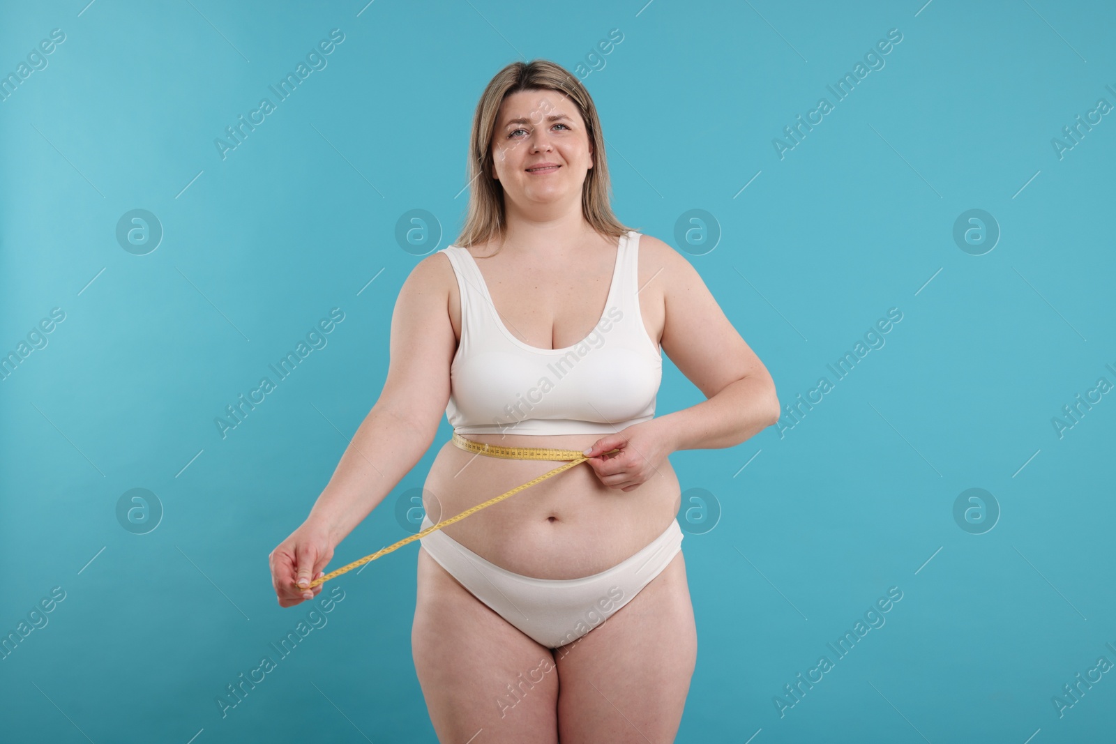 Weight loss. Plus size woman measuring waist with tape on light blue background Photo of Weight loss. Plus size woman measuring waist with tape on light blue background