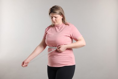 Photo of Weight loss. Plus size woman measuring waist with tape on gray background