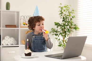 Photo of Little boy celebrating his birthday while having video call via laptop at table indoors