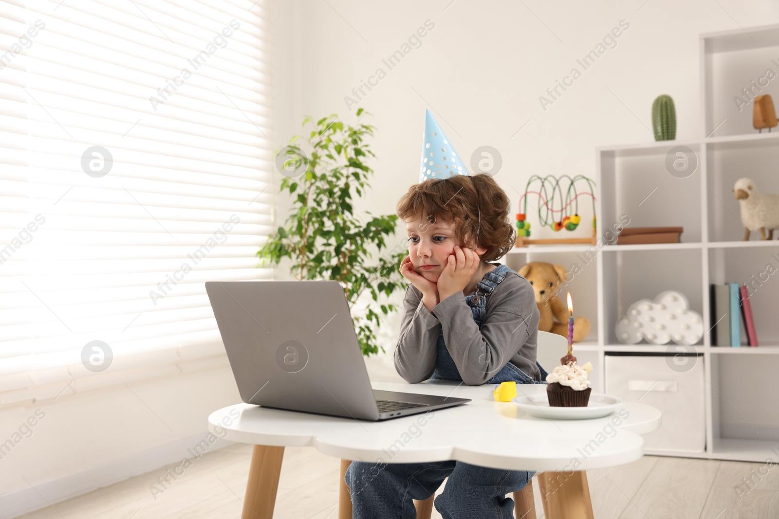 Birthday celebration. Little boy with cupcake having video call via laptop at table indoors Photo of Birthday celebration. Little boy with cupcake having video call via laptop at table indoors