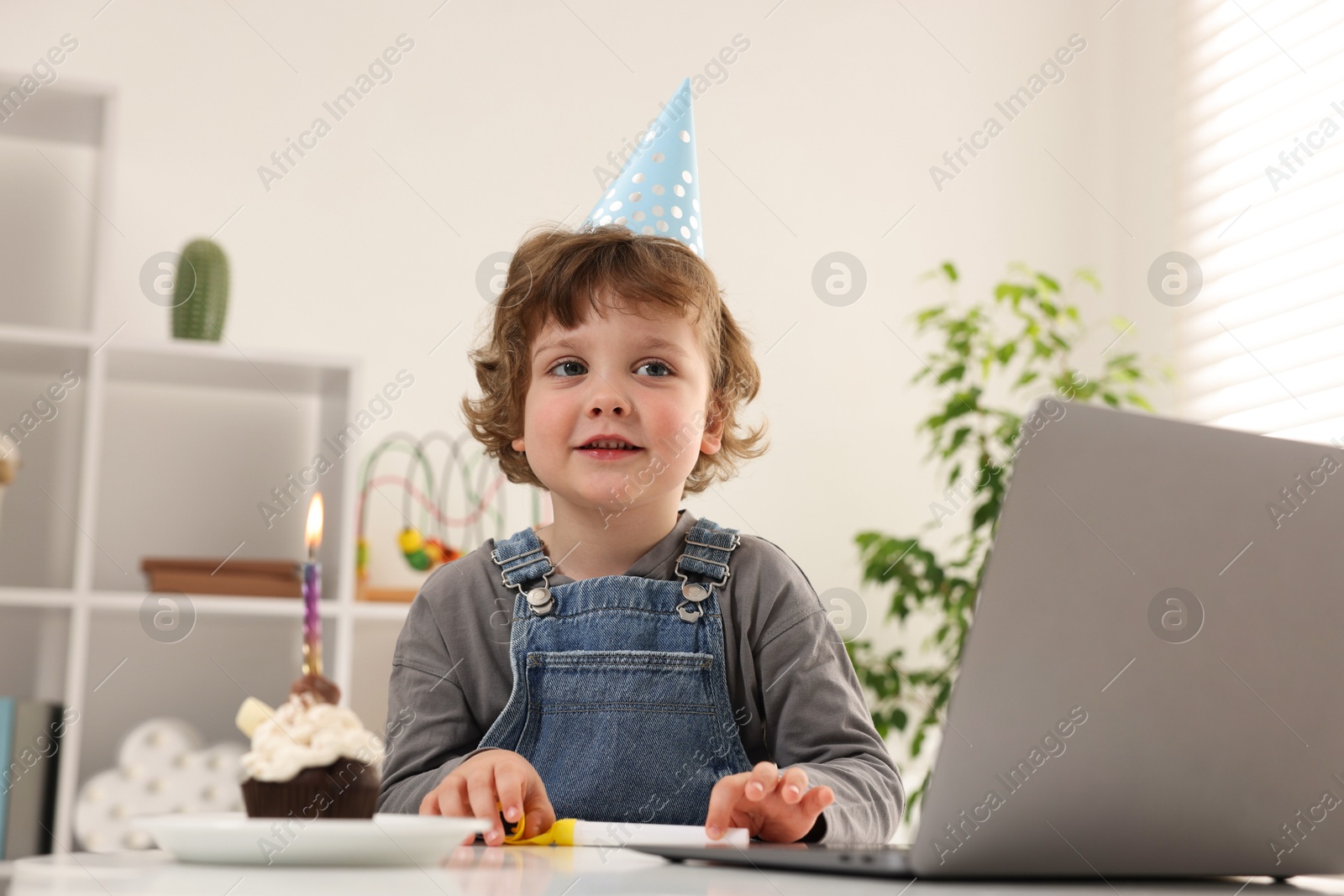 Birthday celebration. Little boy with cupcake having video call via laptop at table indoors Photo of Birthday celebration. Little boy with cupcake having video call via laptop at table indoors