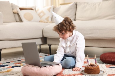 Photo of Birthday celebration. Little boy with cake having video call via laptop at home