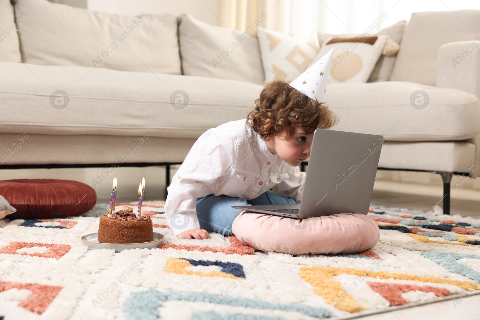 Photo of Birthday celebration. Little boy with cake having video call via laptop at home
